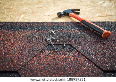 Asphalt shingles on a roof of wood with hammer and nails. focus on nails and roof