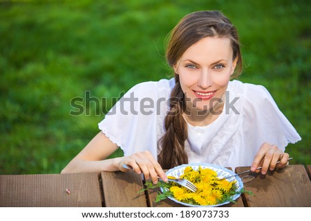 Woman diet concept portrait. Female model eat dandelion salad happy smiling isolated over green grass summer background. focus on face, copy space