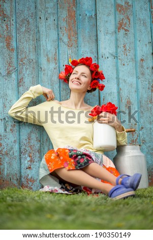 Beautiful happy girl with flowers on head relaxing outdoors over fence blue background