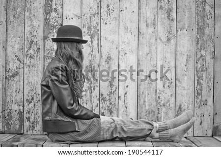 Sad woman deep in thought sitting over grunge wooden background. black and white