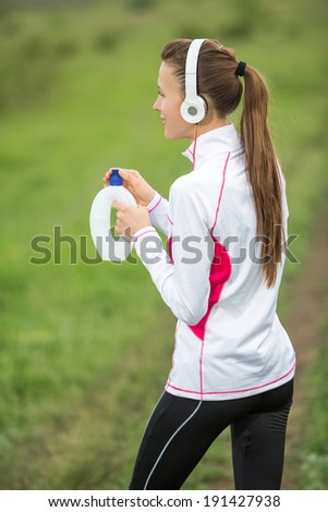 Woman fitness runner drinking water and listening music. Fitness woman relaxing during working out in nature