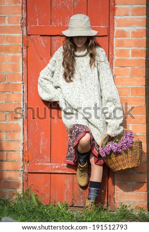 Romantic woman with hat and basket of flowers over grunge bright background looking down. shadows on face from hat
