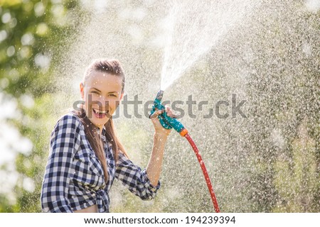 Beautiful young woman having fun in summer garden with garden hose splashing summer rain. soft backlight, motion