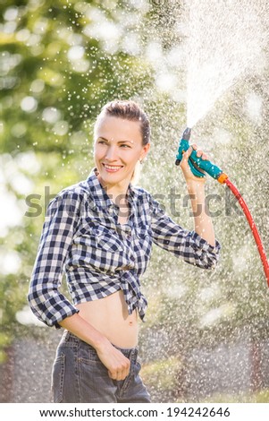 Cheerful woman watering garden lawn, having fun after working in the garden. backlit