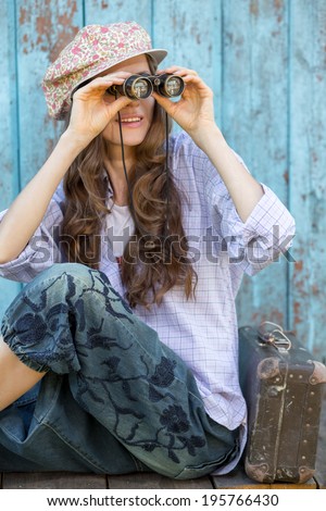Fashion portrait of young pretty woman in cap with binoculars looking to the side. focus on binoculars