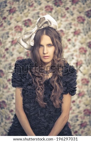 A portrait of a young woman with a grey bow in hair over flower background. retro toned vintage image
