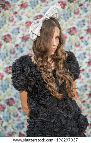 A portrait of a young woman with a grey bow in hair over flower background