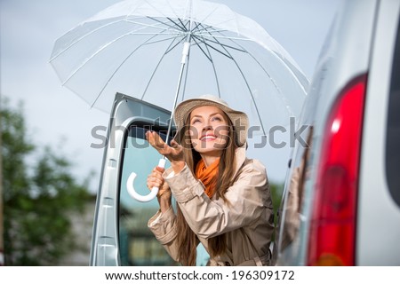 Young happy woman with umbrella go from car.  Happy car traveler concept