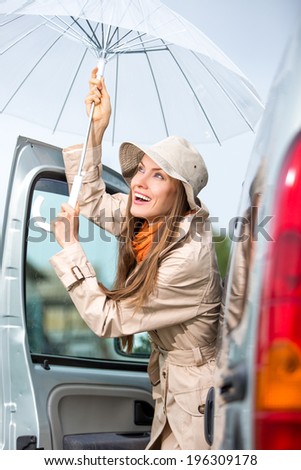 Young happy woman with umbrella go from car. Happy car traveler concept