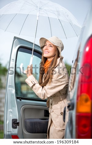 Young happy woman with umbrella go from car. Happy car traveler concept