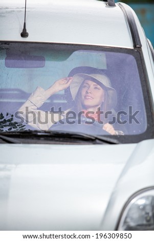 Woman in car indoor keeps wheel turning around smiling looking through window on a rainy day. daylight, focus on face