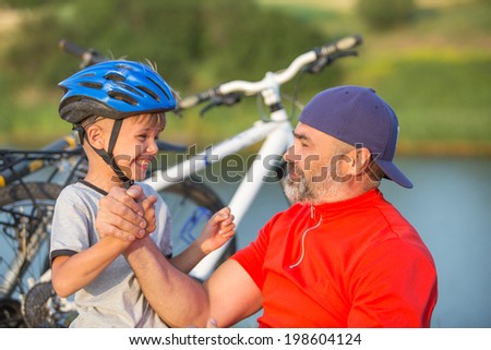 Father and son arm wrestling outdoors with bikes and nature background. focus on hands