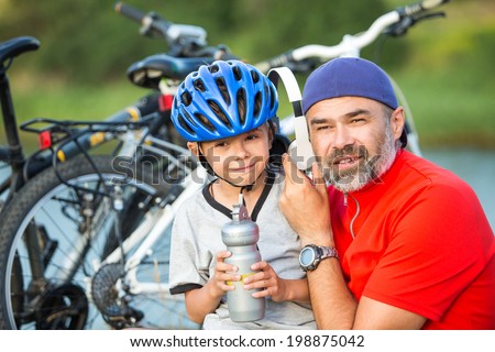 Portrait of a happy father with his little son on vacation. Father and son relaxing listening music after riding bikes