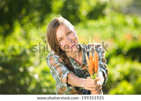 Portrait of happy gardener woman with fresh organic carrots over green natural background. backlit, focus on face