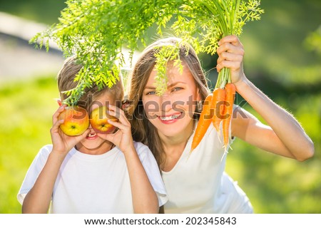 Happy mother and son with vegetables. outdoor shot. focus on mothers face and boys mouth