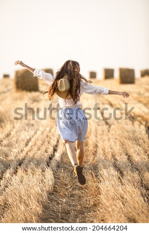 Happy people - free woman enjoying nature sunset. Young woman running on field in motion with outstretched arms
