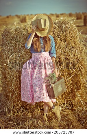 Woman with suitcase. Fashion woman holding old suitcase and hide her face with hat. toned warm colors