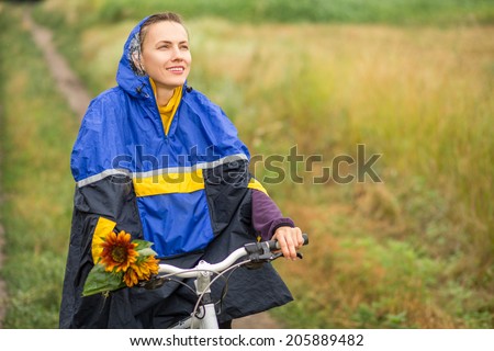 Beautiful smiling girl riding a bike in autumn rainy day