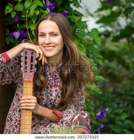 Young woman with guitar over dark green garden background. copy space