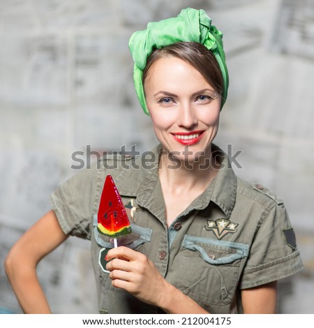 Army military pinup woman with lollipop over dark grey newspaper background.