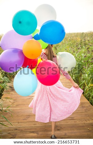 Beautiful woman with colorful balloons walking on wooden bridge. focus on balloons