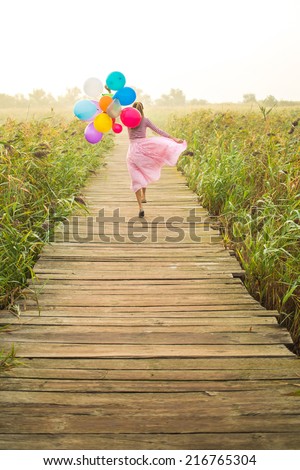 Beautiful woman with colorful balloons walking on wooden bridge road early in foggy morning. focus on balloons