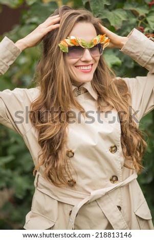 Beautiful autumn woman in raincoat wearing funny sunglasses with autumn leaves decor. soft daylight