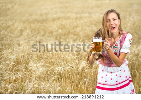 Young sexy woman wearing a dirndl with beer mug over wheat field. soft daylight