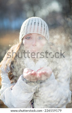 Portrait of a young girl in winter forest blowing snow. backlight, focus on eyes