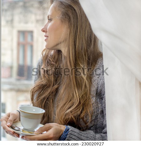beautiful girl enjoying the freshness of the new day, drinking morning tea of coffee by the window