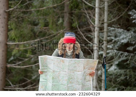 Hiking woman in autumn or winter nature holding map outdoors over dark forest. daylight focus on face