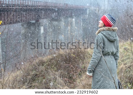 First snow concept. Young traveler enjoy her journey relaxing outdoors with beautiful falling snow and old bridge at the background. toned image