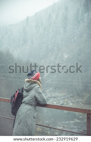 Mountain hiking. Young hiker standing on bridge and admire beautiful winter mountain landscape. toned vintage dark image