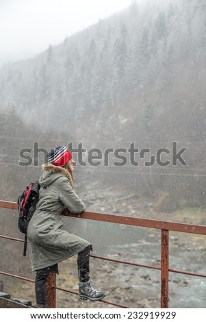 Woman hiker trekking in mountains, relaxing on bridge looking on beautiful winter mountains