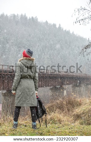 Woman hiker trekking in mountains, relaxing standing and looking on first snow falling