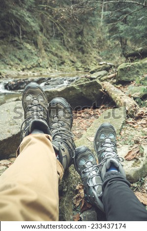 two hikers legs on a hiking path relaxing near mountain waterfall in autumn nature. focus on man boots. toned