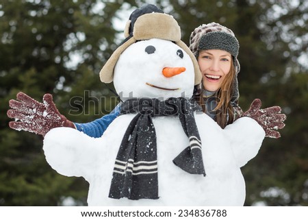 Carefree winter funny young woman with snowman and dark forest on the background