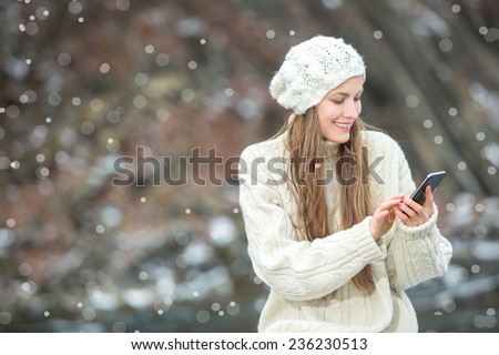 Young  woman smiling with smart phone and winter landscape and snowflakes on the background