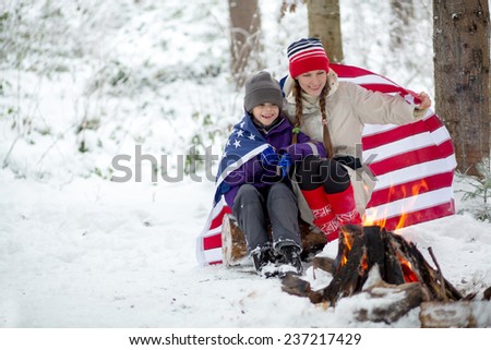 Happy mother and son laughing together outdoors in winter landscape wrapped in american flag. daylight
