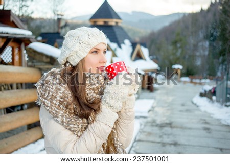 Beautiful girl resting and drinking coffee or tea in winter resort in mountains looking tothe side. Sunset
