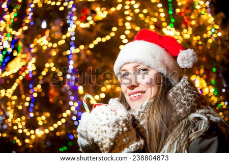 Santa claus beautiful woman drinking hot tea or coffee over christmas tree at night