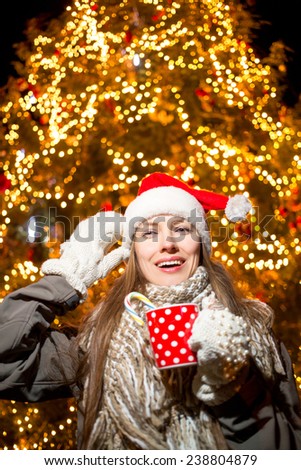 Santa claus beautiful woman drinking hot tea or coffee over christmas tree at night