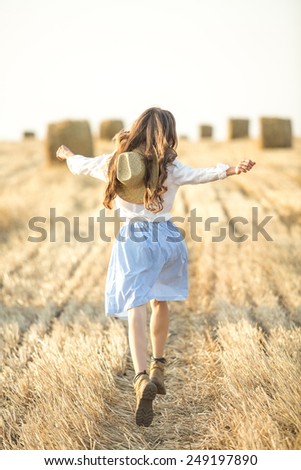 Young woman running on field in motion with outstretched arms, motion, soft daylight