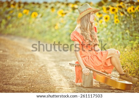 Beautiful traveler in rural scenery sitting on suitcase. toned old vintage image, sunshine, soft backlight