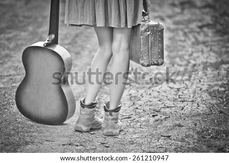Legs of a woman traveler with suitcase and guitar standing on rural road. black and white, toned vintage image, vignette,  copy space
