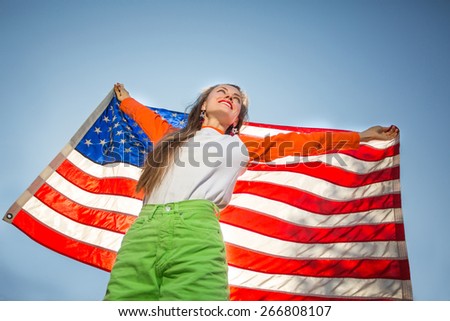 Beautiful young pretty woman with national usa flag over blue sky, backlight, focus on face