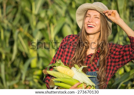 Female farmer or gardener in a hat holding corn, fresh vegetables. Agriculture - food production, harvest concept