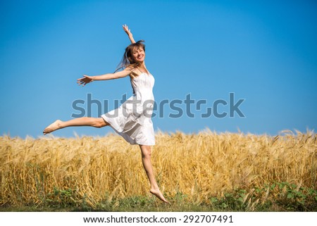 happy girl running jumping carefree with outstretched hands over yellow field and blue sky