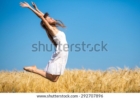 happy girl running jumping carefree with outstretched hands over yellow field and blue sky