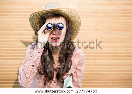 Beautiful woman looking up with binoculars over wooden background . focus on binoculars